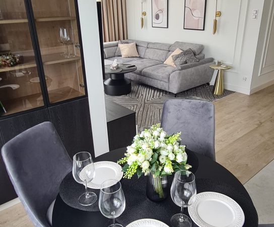 Open plan kitchen / dining / living room with glod accents, black round dining table and grey chairs - Modern Apartment interior design in Warsaw, Poland