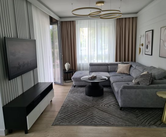 Cozy living room in neutral colours with grey sofa and feature wall and wooden floor - modern apartment interior design in Warsaw