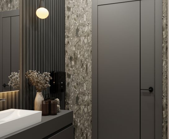 Contemporary men's restroom with a dark gray vanity, white counter sink, large terrazzo-style stone wall, dark door, and hanging pendant lights.